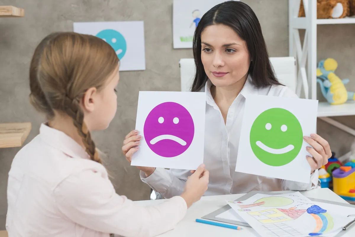 Close up girl choosing sad face emoticons paper held by smiling young